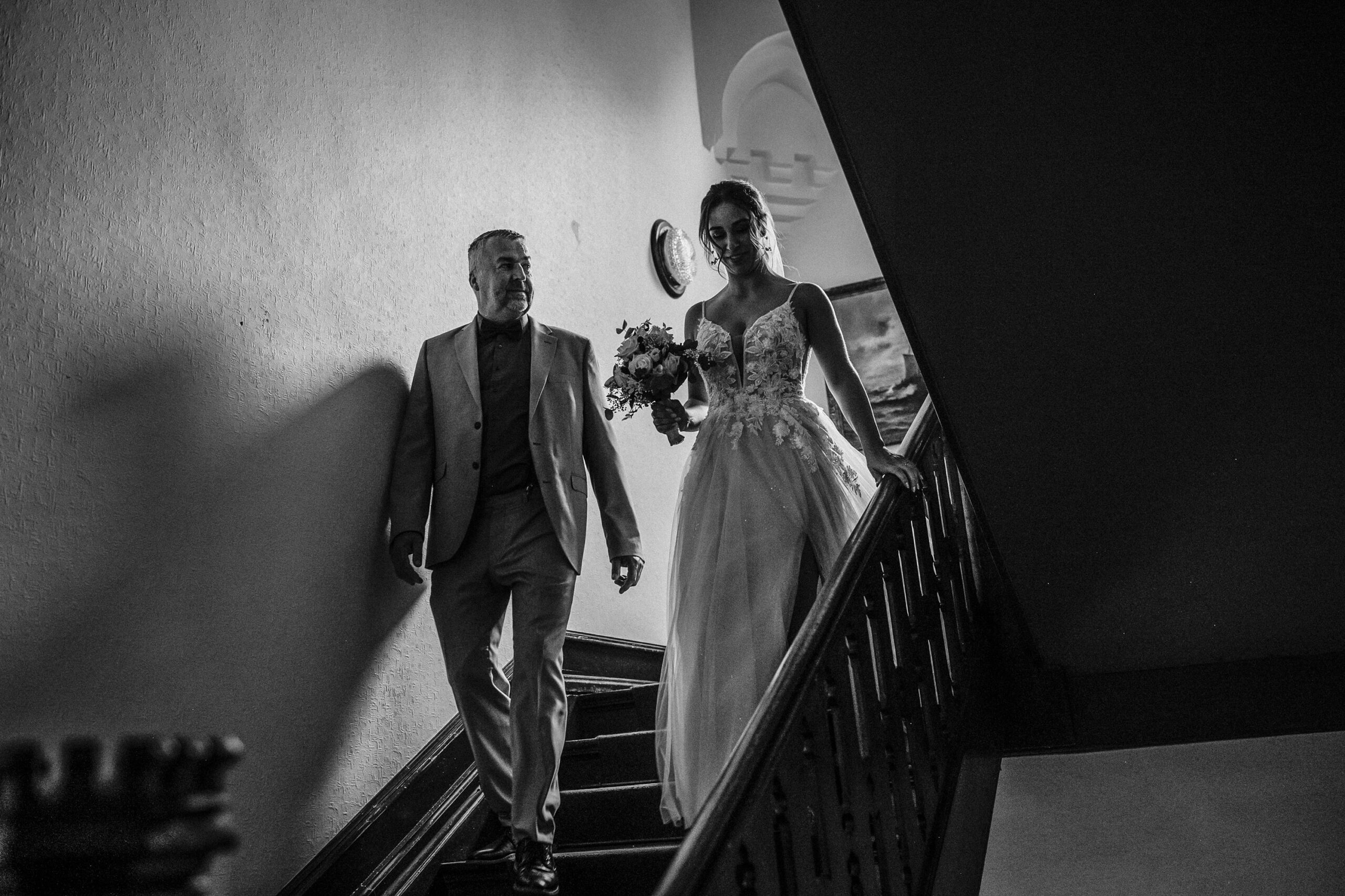 Braut im Hochzeitskleid und Mann im Anzug gehen Treppe hinunter, Schwarz-Weiß-Foto.