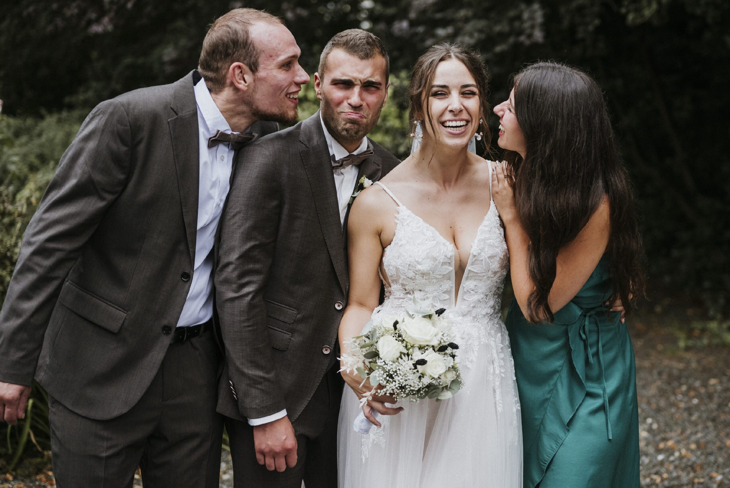 Braut, zwei Männer in Anzügen, Frau im grünen Kleid, alle lachen.