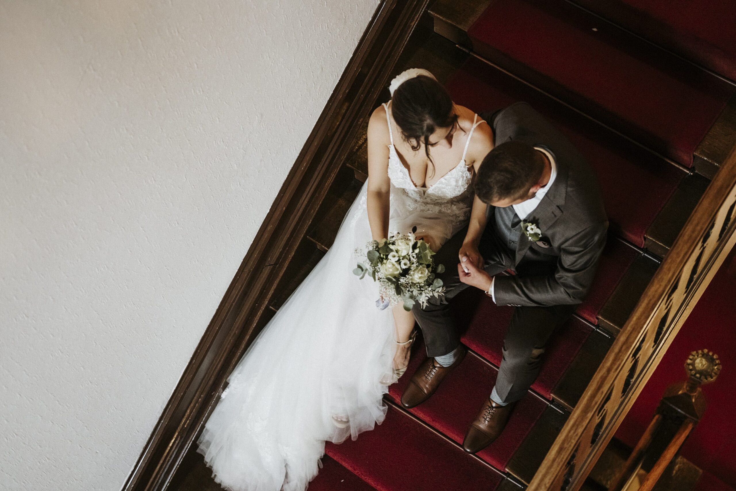 Brautpaar auf roter Treppe, Braut mit Blumenstrauß, beide schauen nach unten.