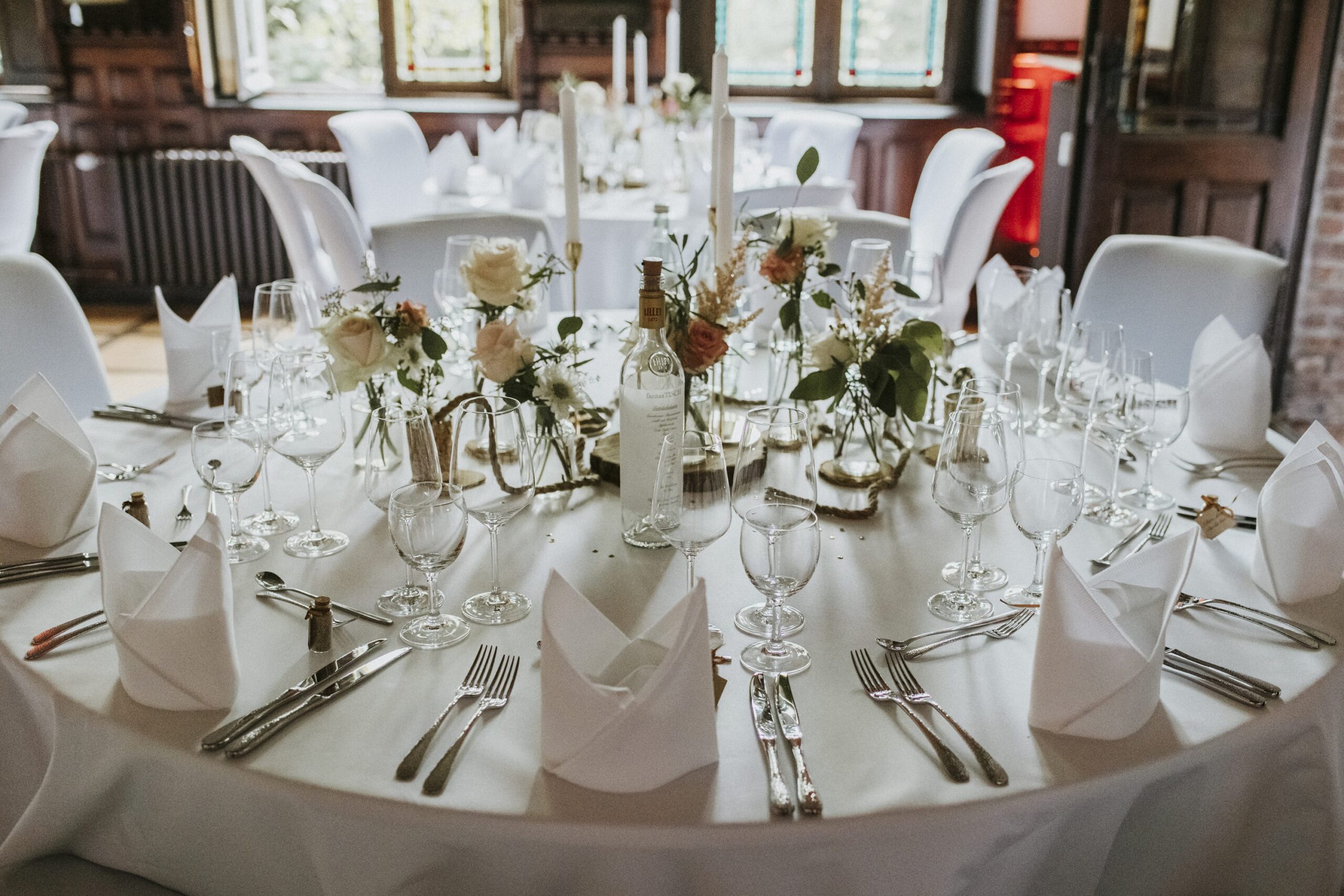 Eleganter runder Tisch mit weißen und rosa Blumen, Kerzen und gedecktem Geschirr.