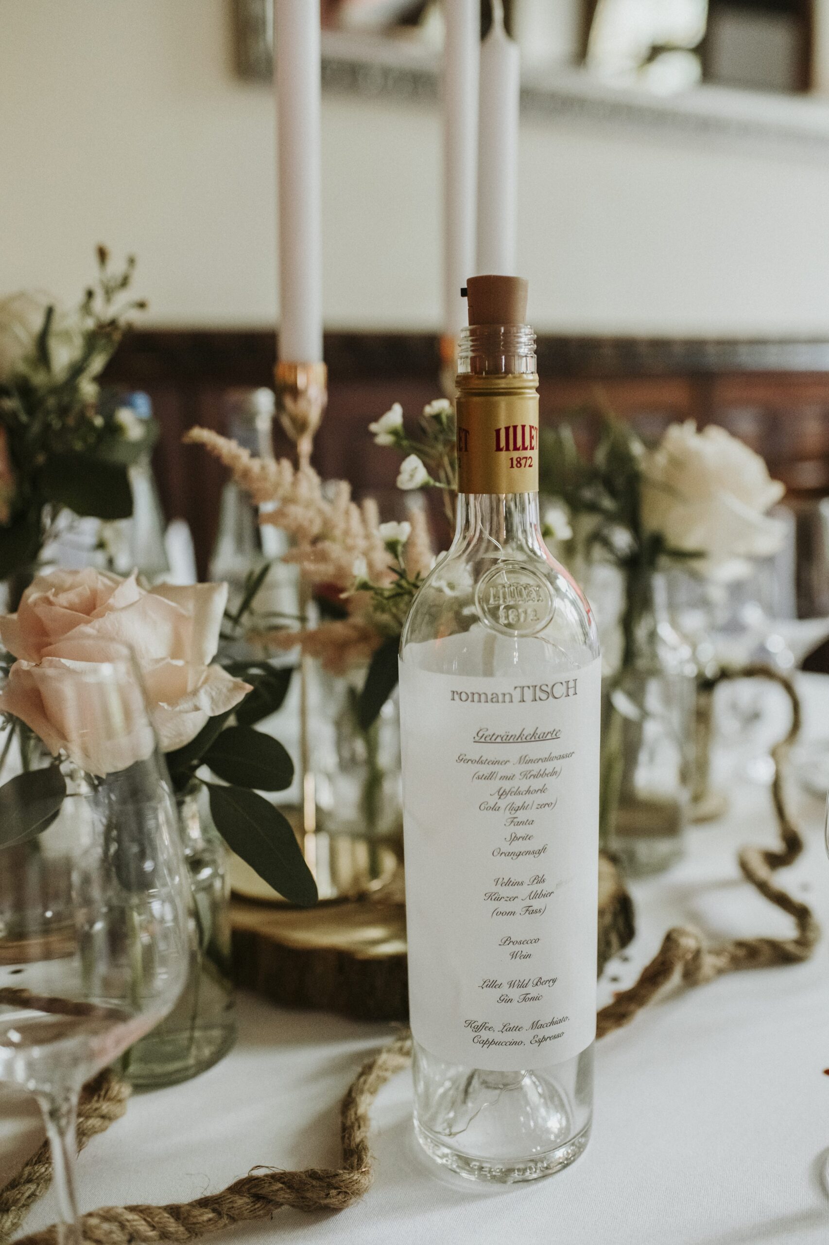 Festlich gedeckter Tisch mit Getränkekarten-Flasche, Blumen, Kerzen und Gläsern.