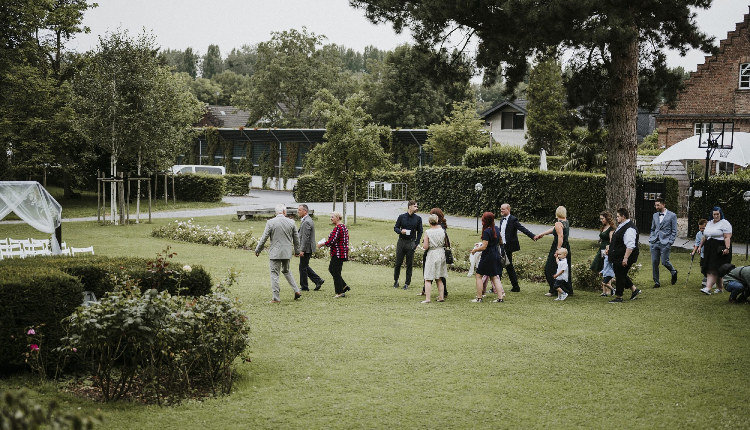 Gruppen von Leuten in festlicher Kleidung auf einer Gartenveranstaltung mit weißen Stühlen im Freien.
