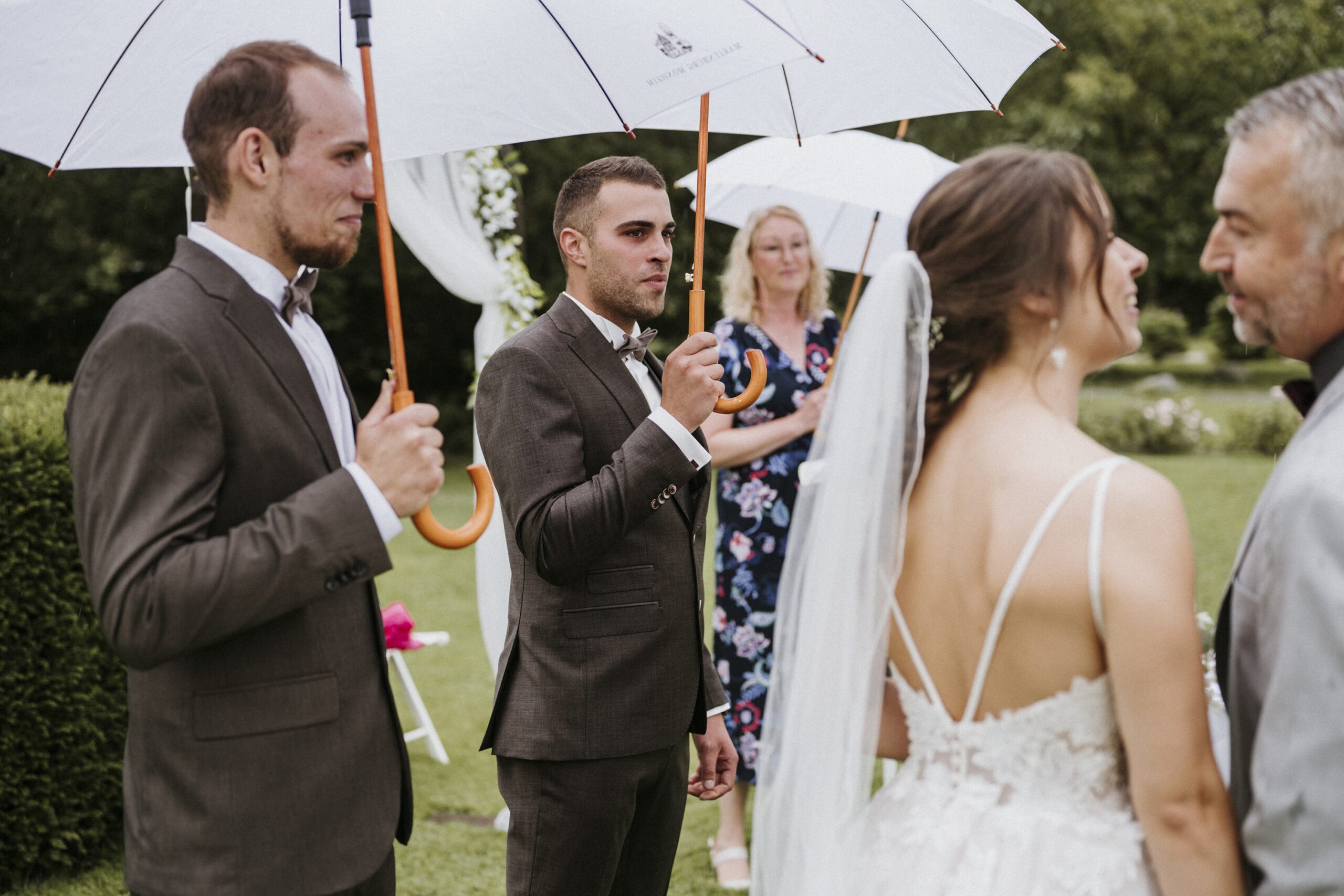 Hochzeit im Freien, Brautpaar mit Schleier und Regenschirme, Gäste im Hintergrund.