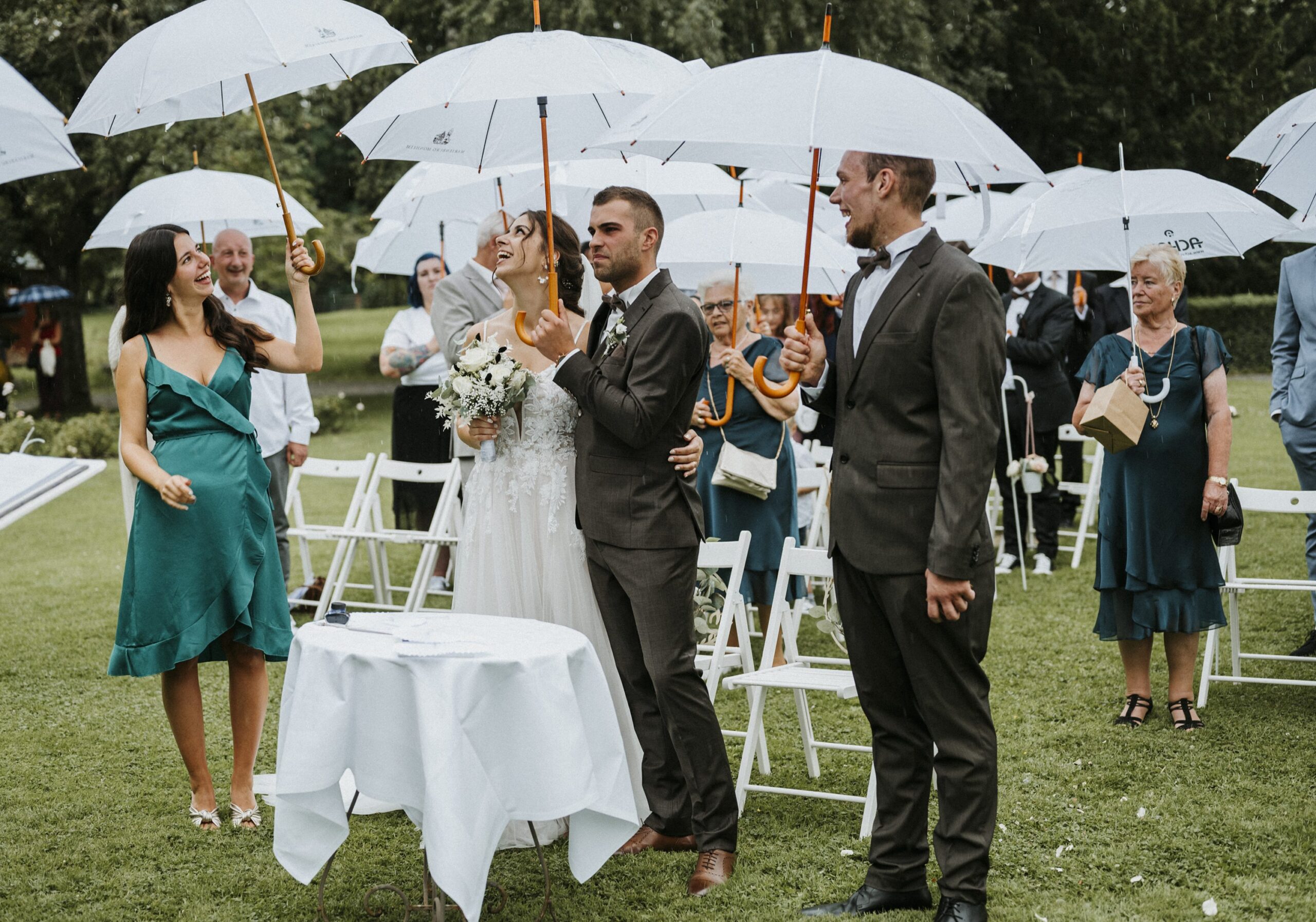 Menschen mit weißen Regenschirmen bei einer feierlichen Hochzeit im Freien, leichtem Regen.
