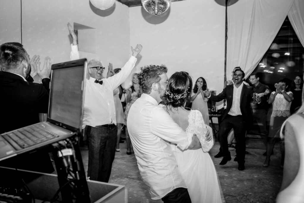 Hochzeitstanz eines Paares in festlichem Raum, Gäste jubeln, Laptop im Vordergrund sichtbar.