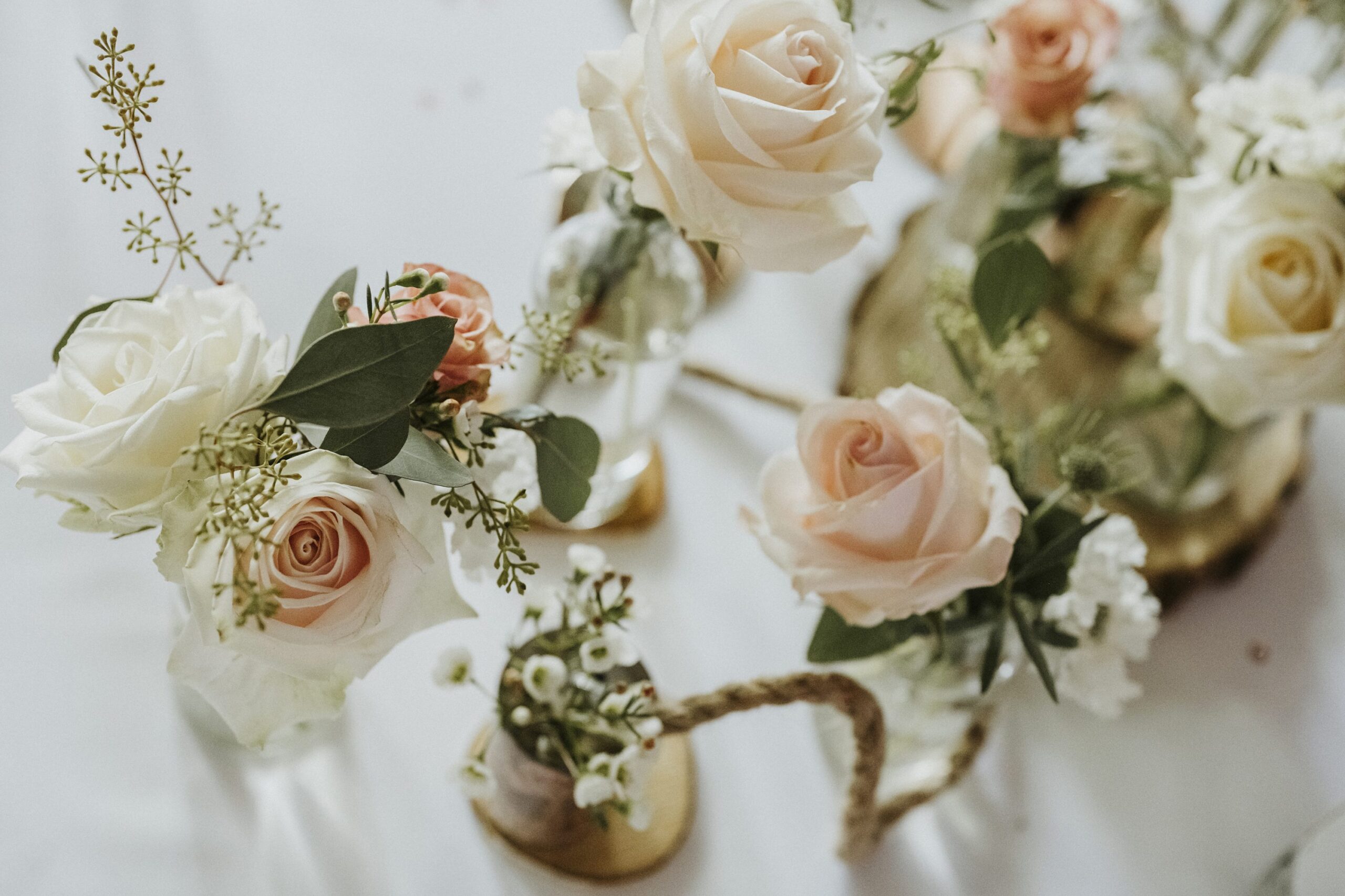 Anordnung pastellfarbener Rosen und weißer Blüten in Glasvasen mit grünen Blättern.