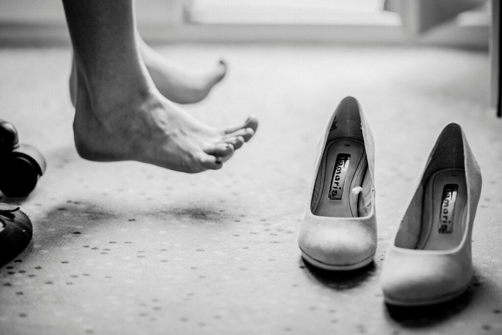 High Heels von Tamaris auf Teppich, barfüßiger Vordergrund sichtbar, Schwarz-Weiß-Fotografie.