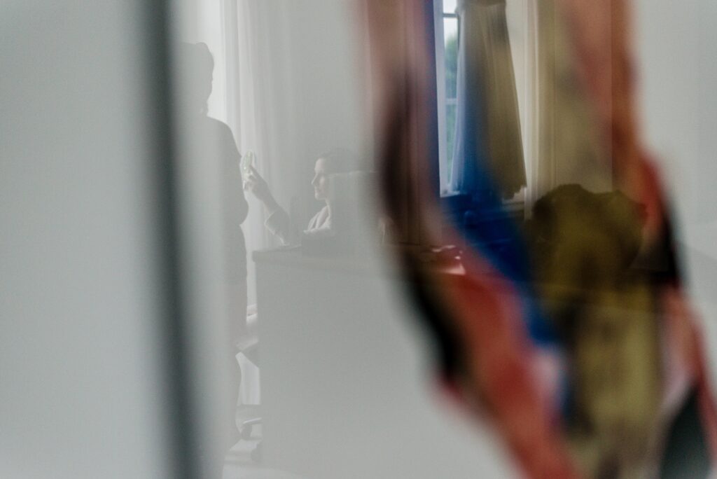 Verschwommene Szene mit zwei Personen in einem Raum, eine hält ein Objekt nahe eines Fensters.