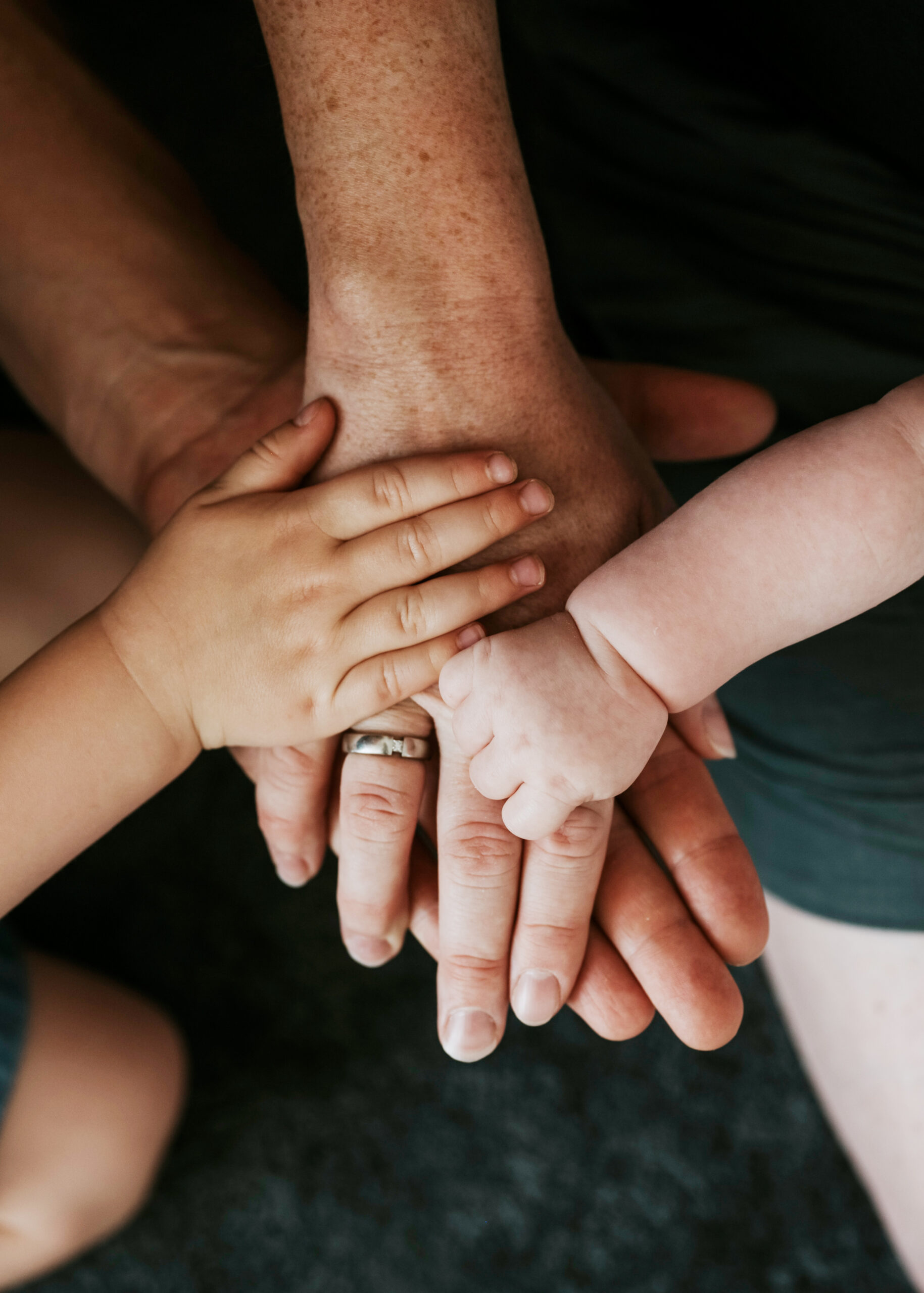 Mehrere sich überlagernde Hände verschiedener Altersgruppen, darunter eine Baby- und Kinderhand.