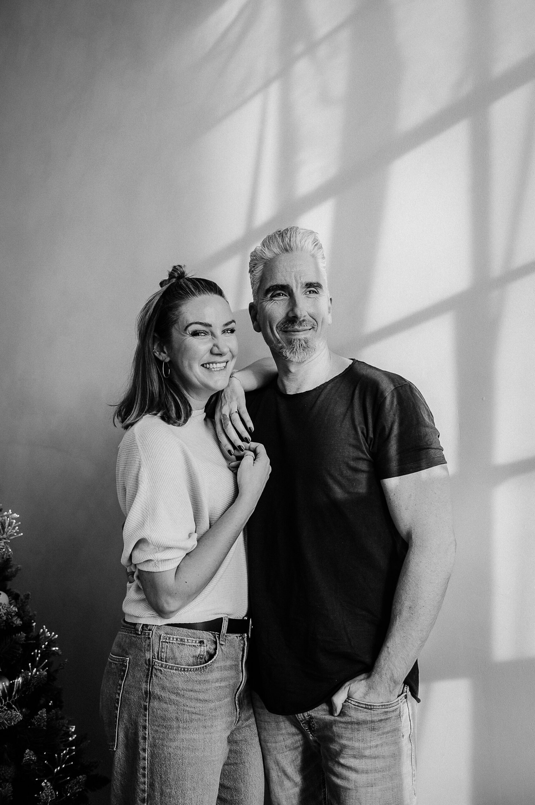 Frau und Mann lächeln nebeneinander, mit Schatten und Baum im Hintergrund.