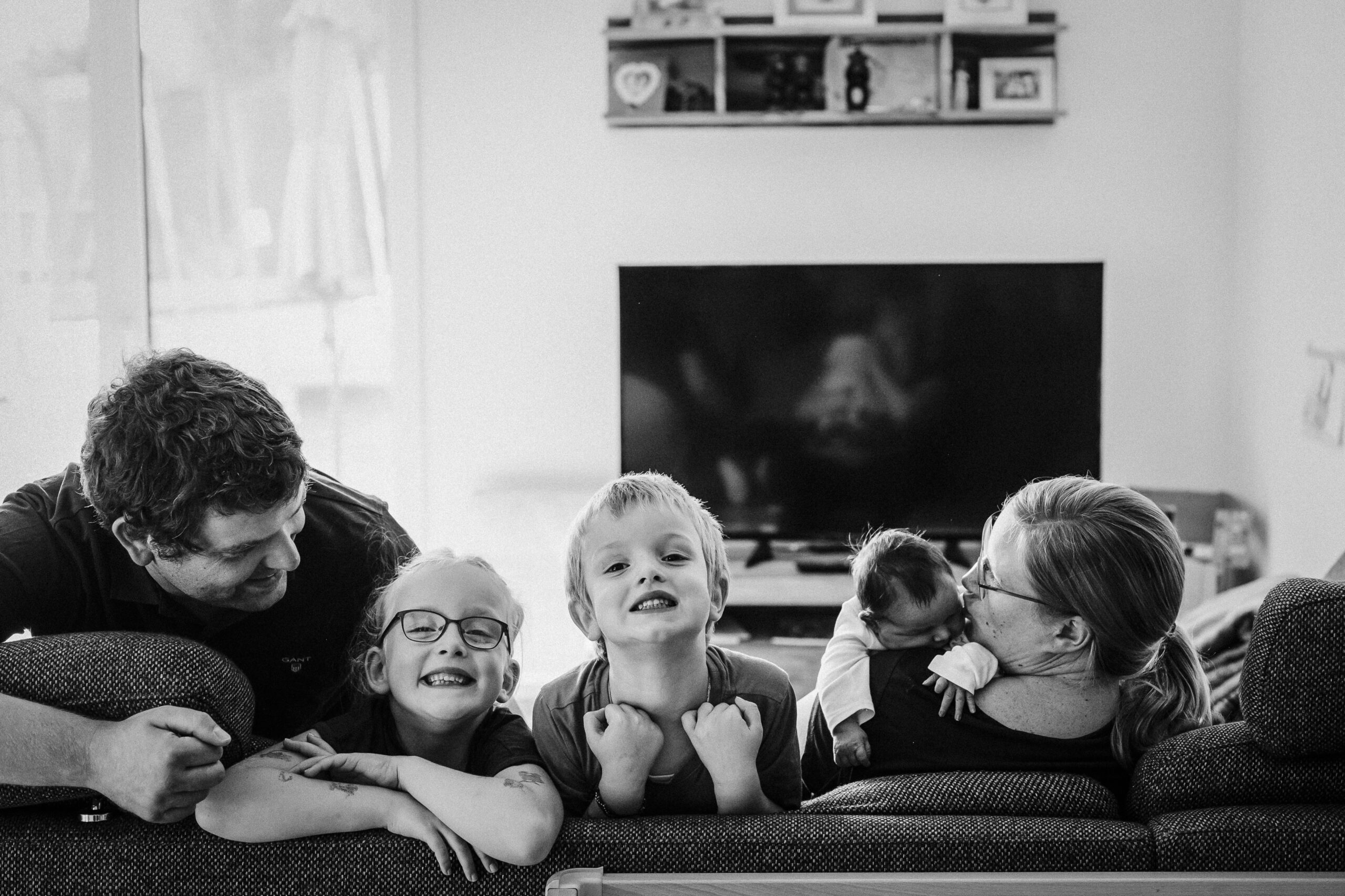 Kinder lächeln im Vordergrund, Eltern interagieren, Baby, TV im Hintergrund.