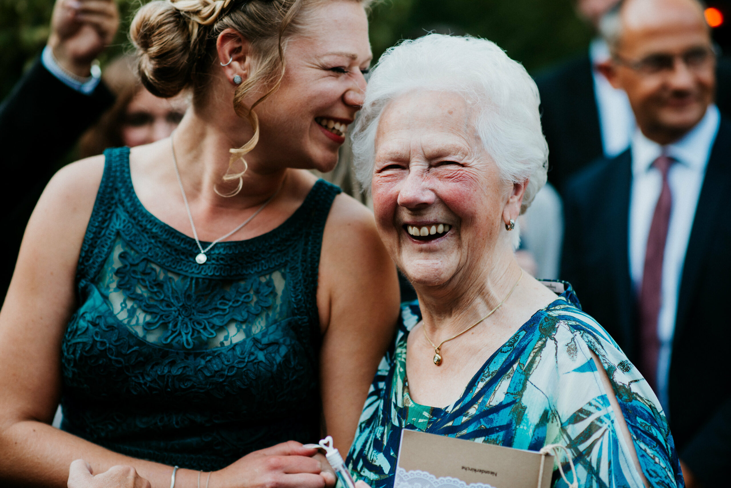 Two smiling women, one older and one younger, at an outdoor festive gathering.
