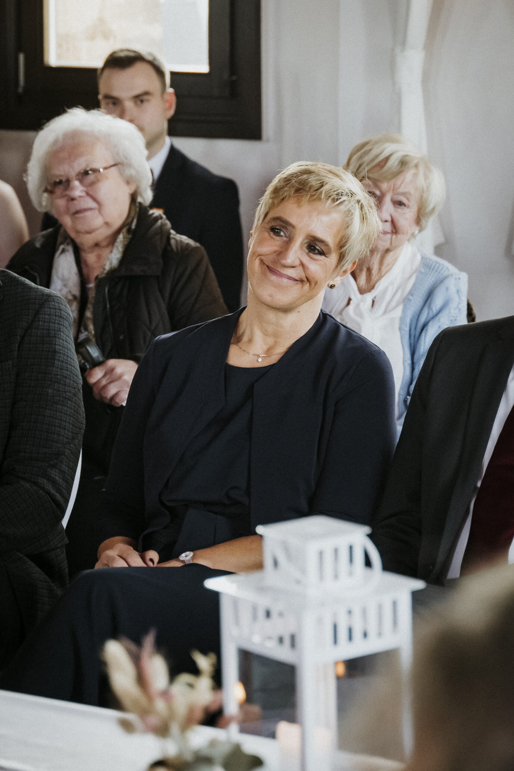 Personen sitzen aufmerksam in einem kerzendekorierten Raum, im Vordergrund eine Laterne.