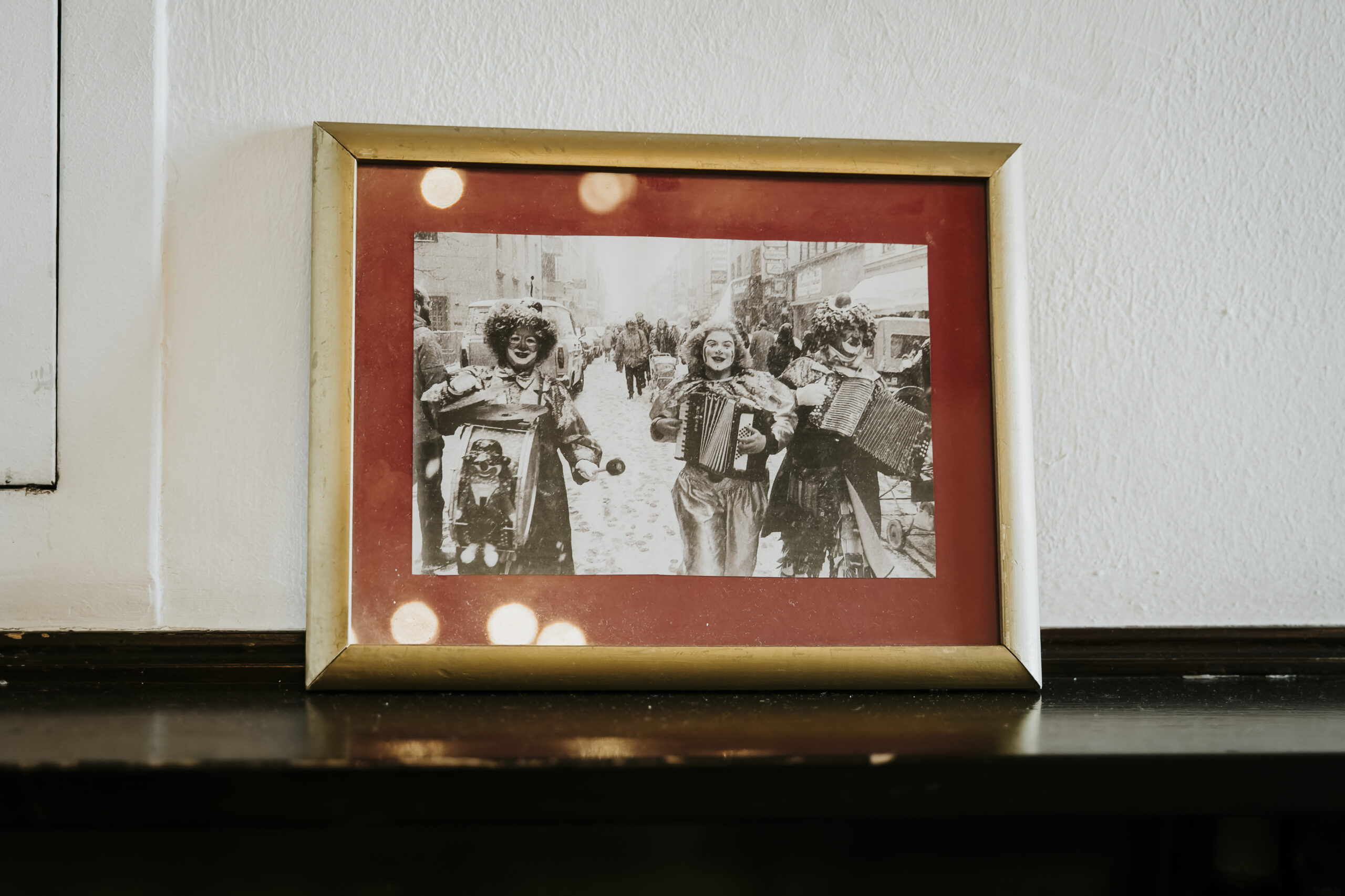 Framed black-and-white photo of three costumed musicians on a snowy street, on a dark shelf.