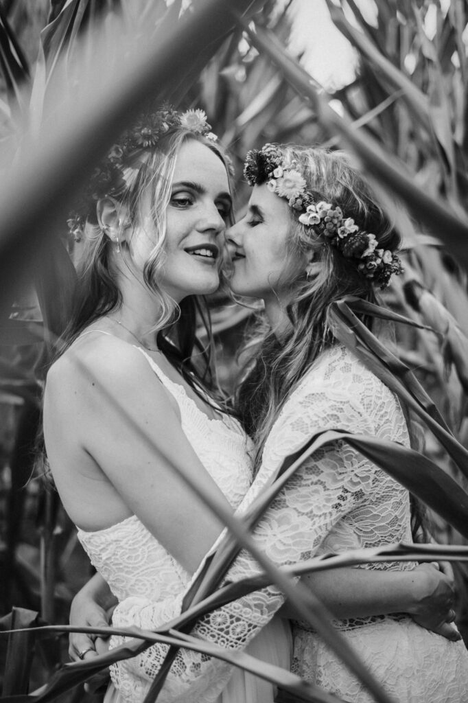 Two people with flower crowns embrace in a field, wearing lace dresses, black-and-white photo.