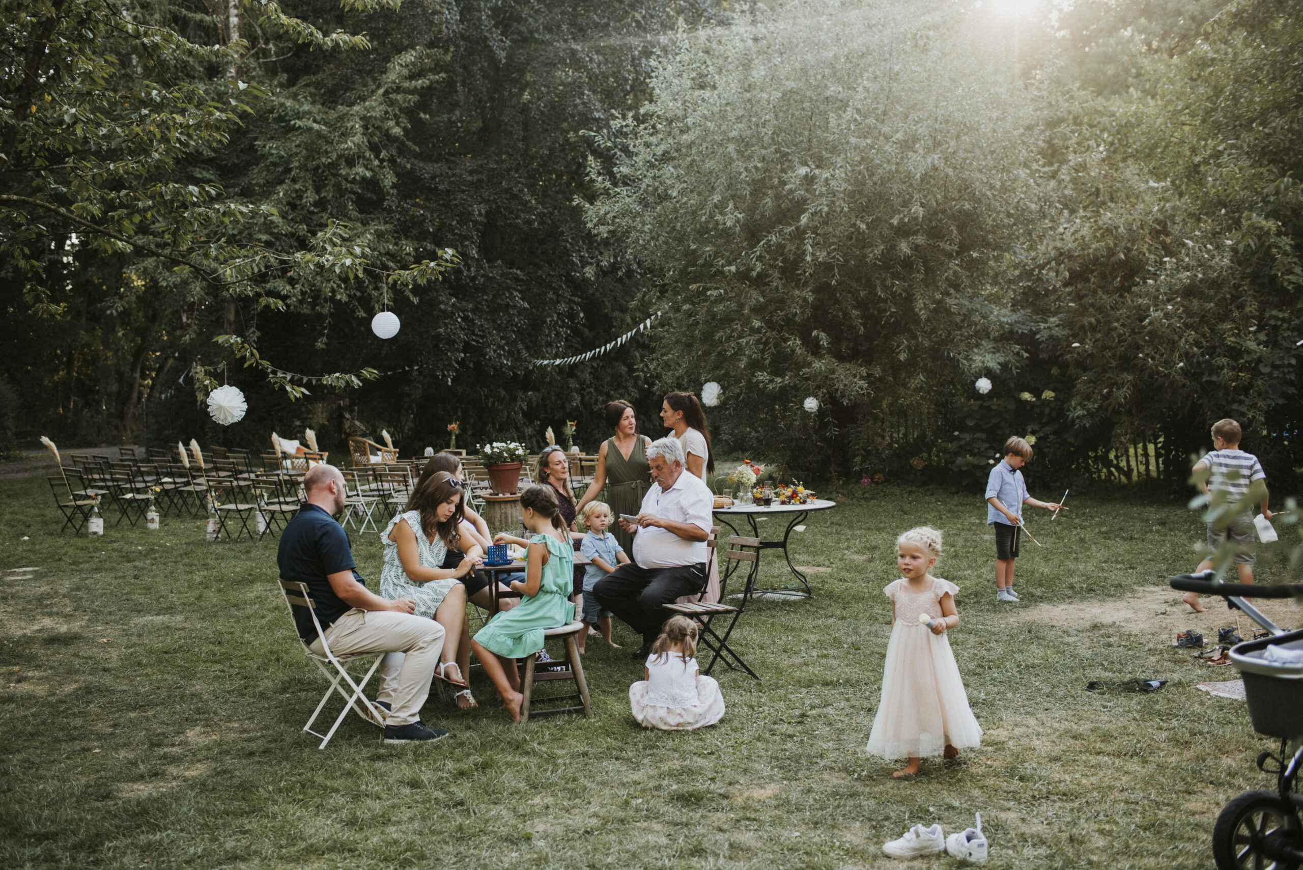 Erwachsene und Kinder bei Gartenfeier im Freien mit Bäumen und Papierlaternen.