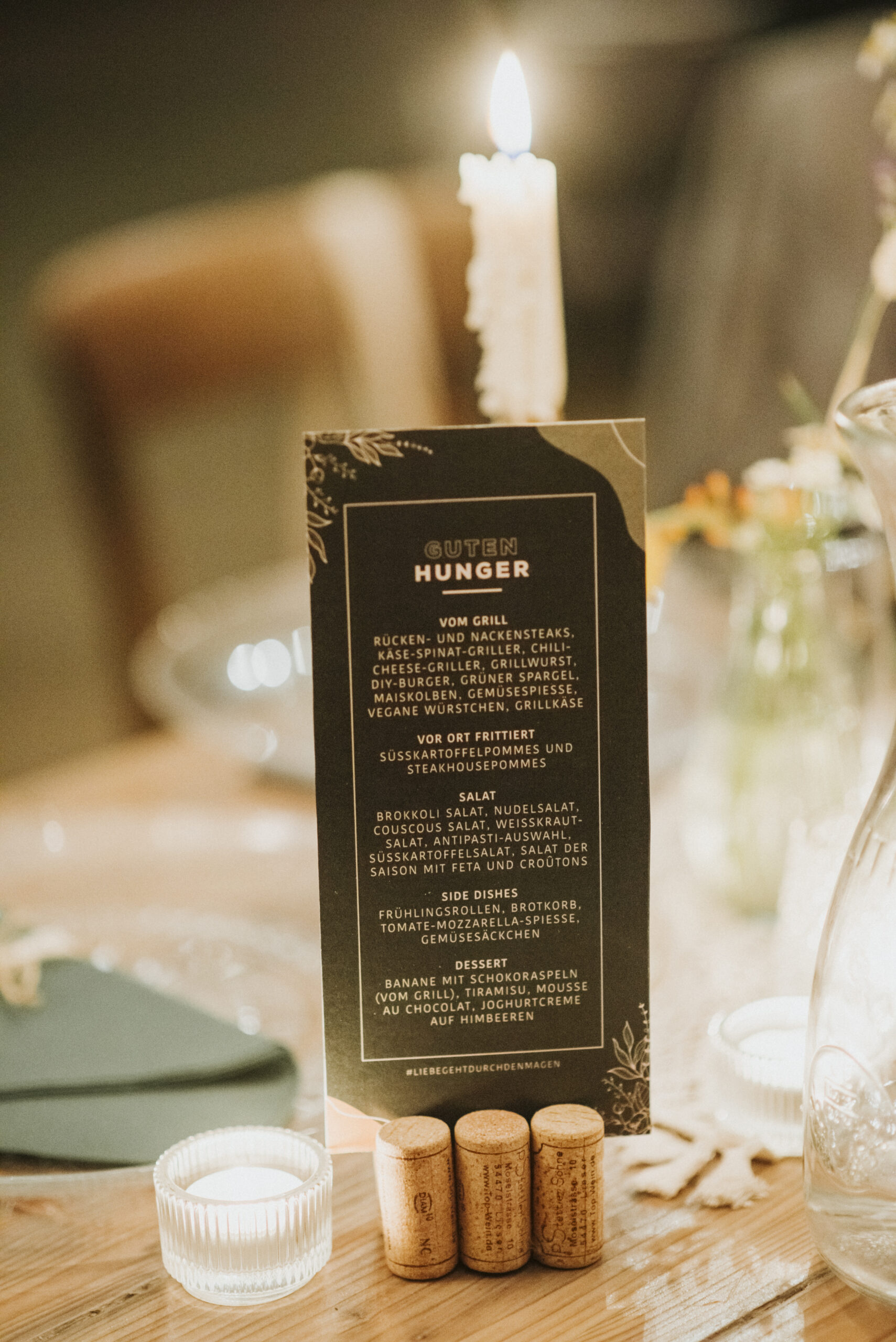 Menü auf Tisch mit Grillgerichten, Salaten, Desserts, brennender Kerze und Glaskerzenhalter.
