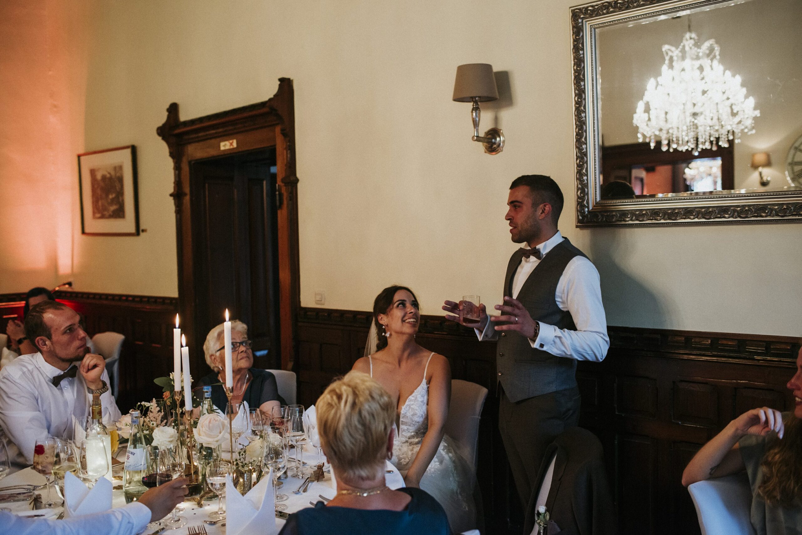 Hochzeit mit Rede, Braut und Bräutigam in elegantem Raum, Gäste hören zu.