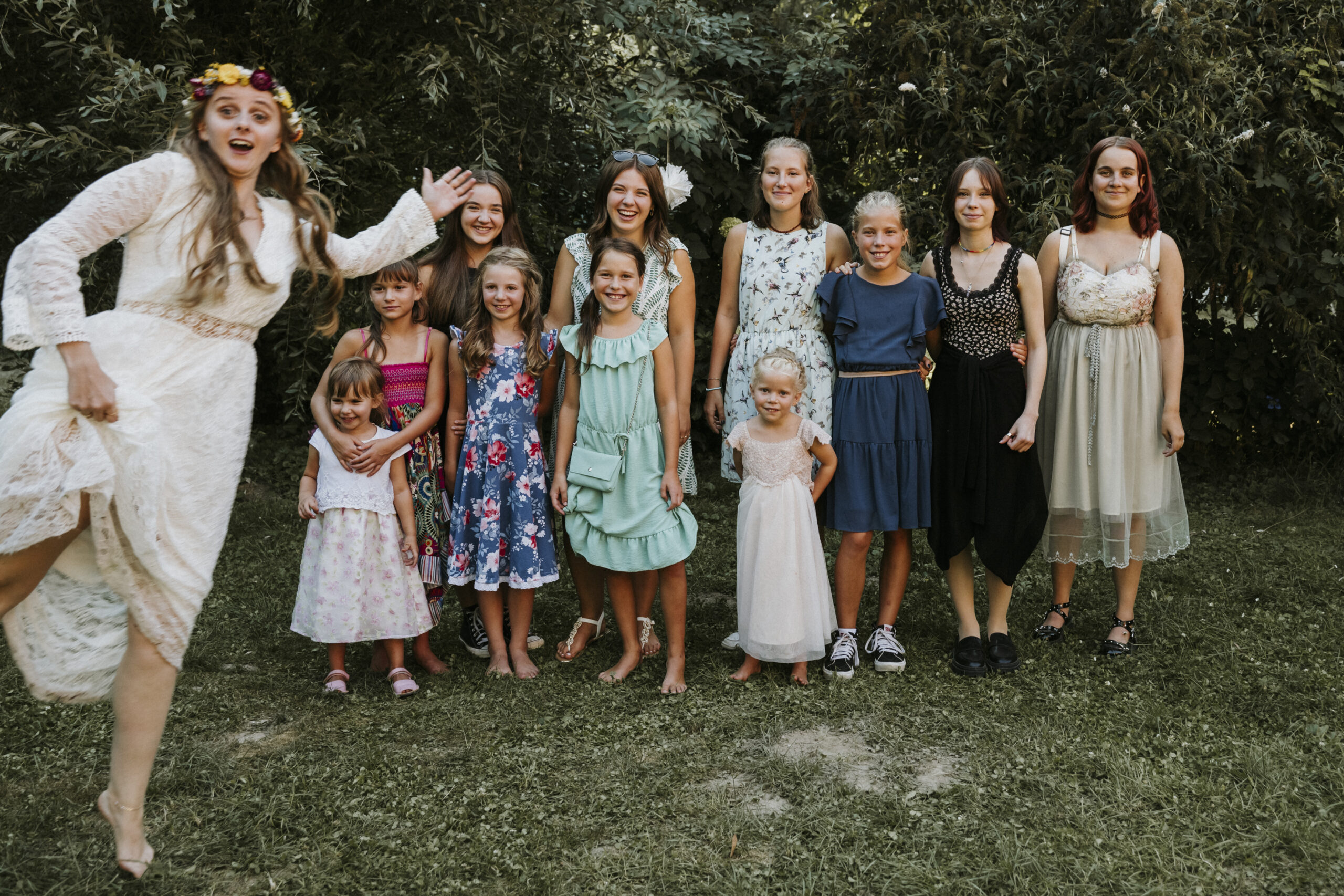 Gruppe junger Frauen und Mädchen in Sommerkleidern auf Wiese vor grünen Büschen.
