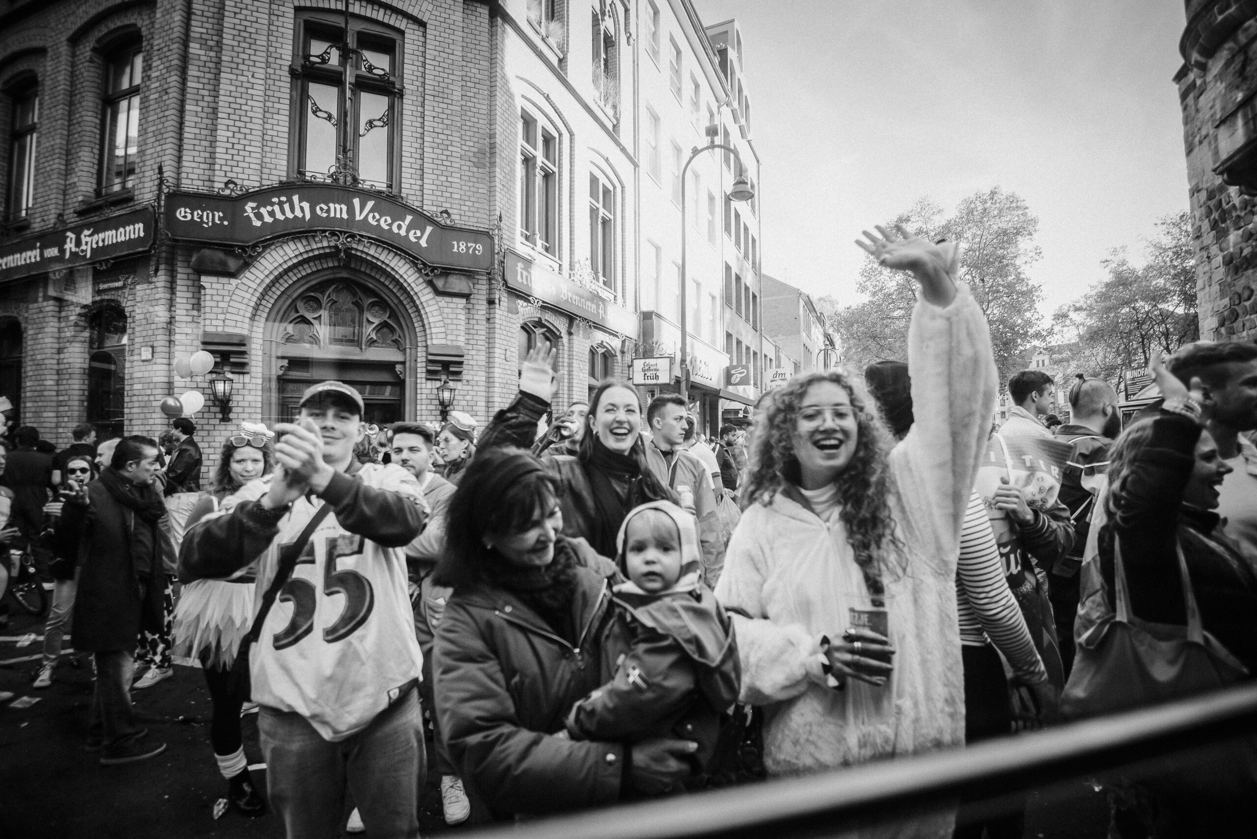Gruppe verkleideter Menschen vor „Früh im Veedel“ bei Straßenveranstaltung, Bäume im Hintergrund.