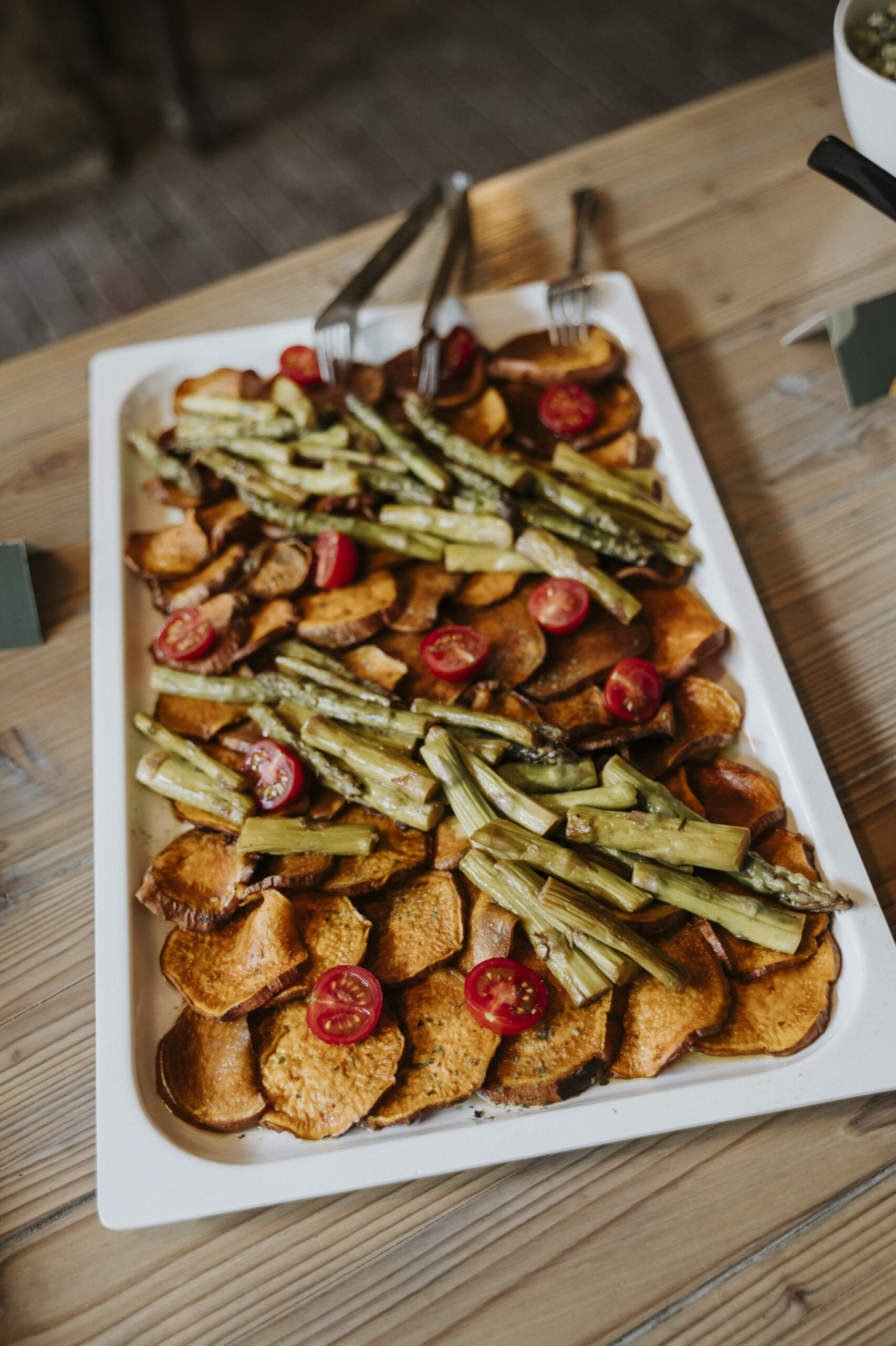 Rechteckiger Teller mit Süßkartoffeln, gegrilltem Spargel und Kirschtomaten auf Holztisch.