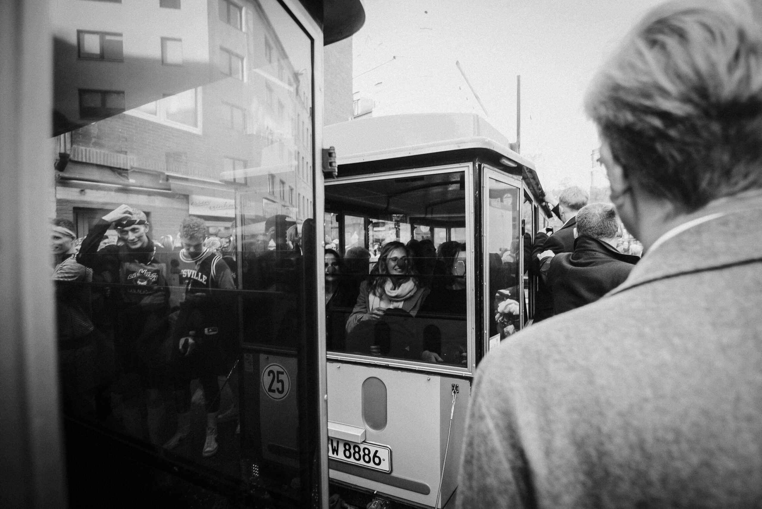 Personen nahe Straßenbahn; einige im Inneren sichtbar, andere draußen stehend, städtische Umgebung.