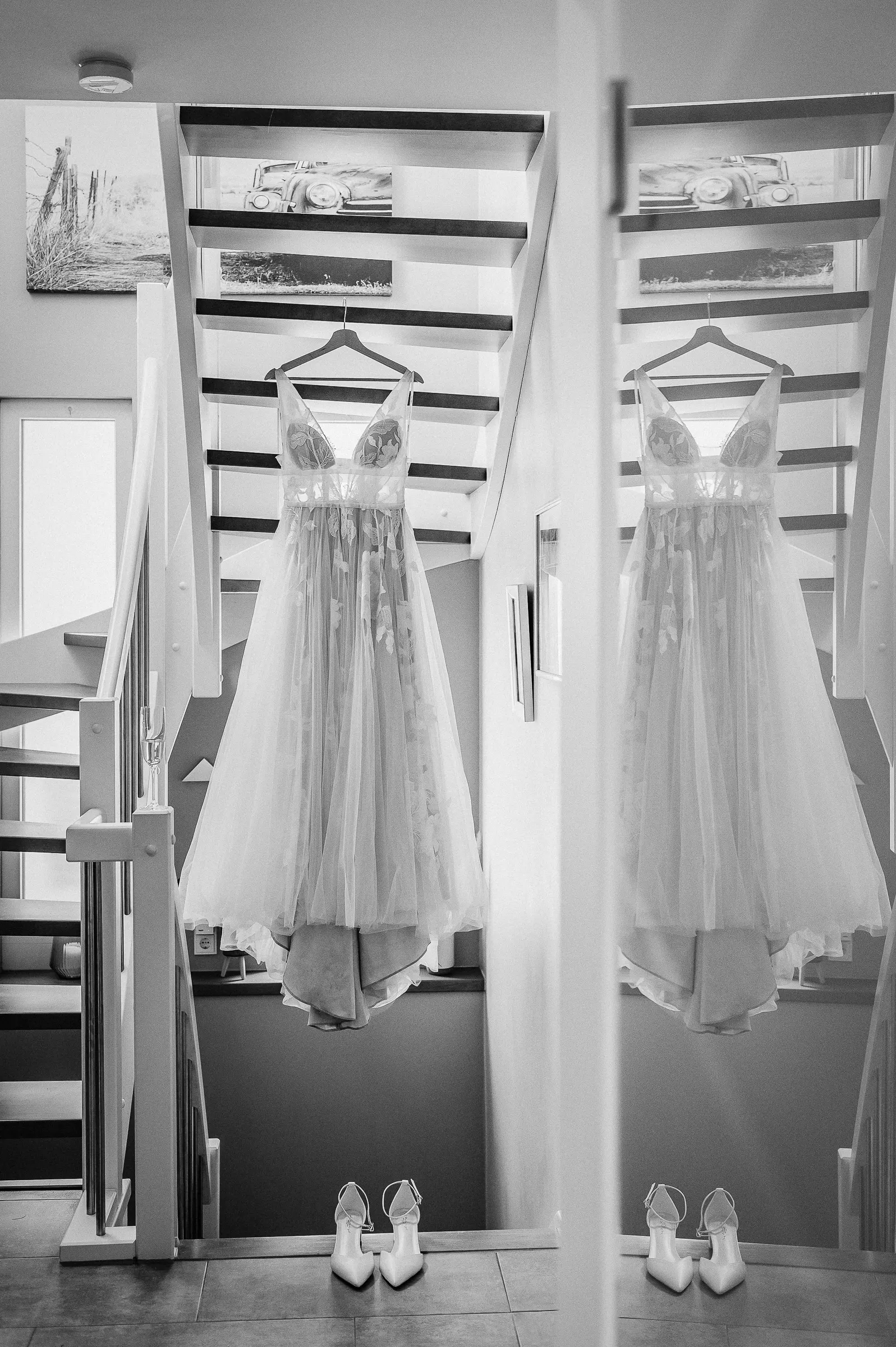 Zwei Brautkleider hängen an Haken vor einer Spiegelwand, darunter weiße High-Heels am Boden.
