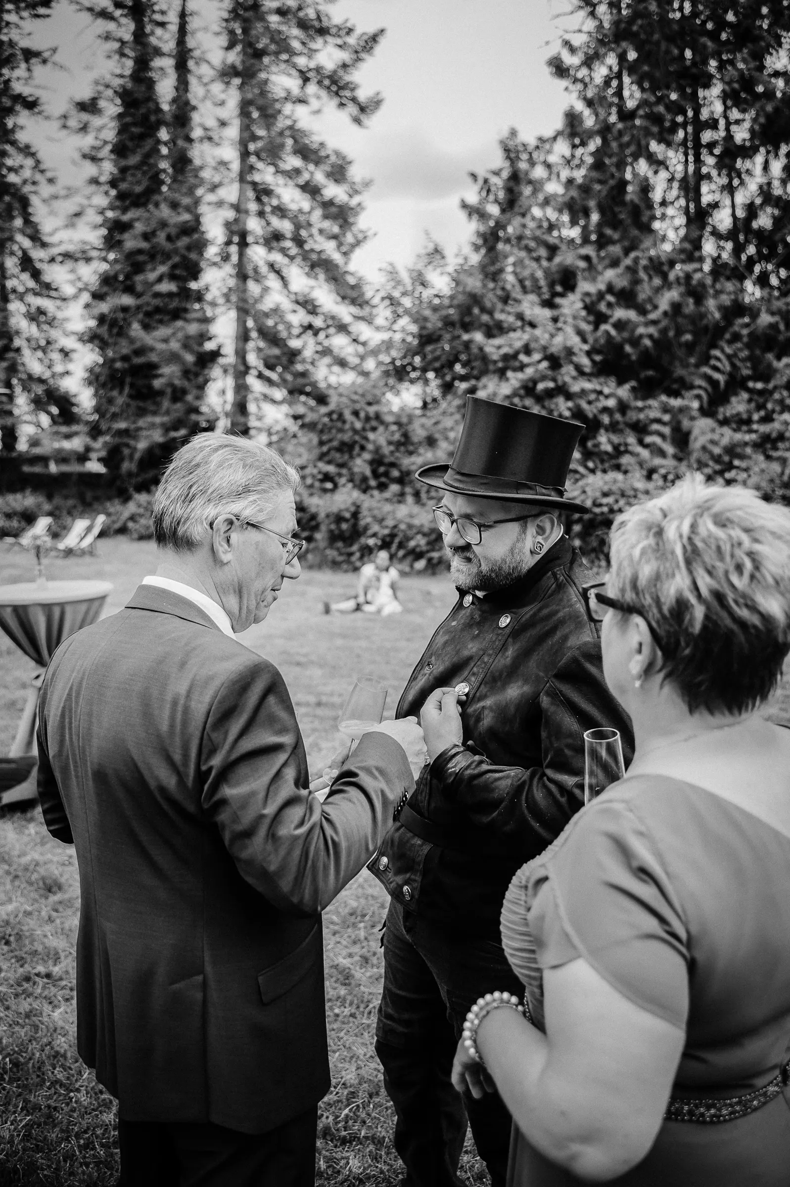 Drei Menschen im Garten bei gesellschaftlicher Veranstaltung im formellen Outfit, Gesprächspartner.